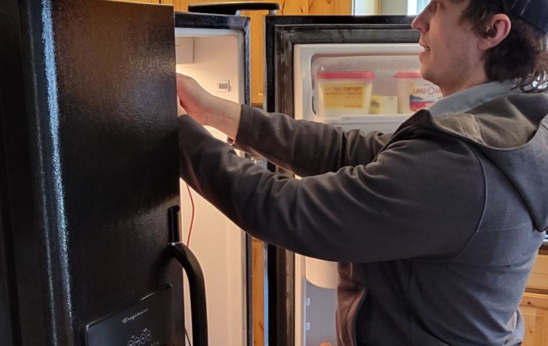A man is opening a refrigerator door in a kitchen.