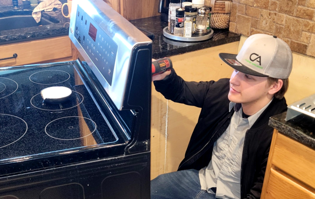 A boy wearing a hat is sitting in front of a stove.
