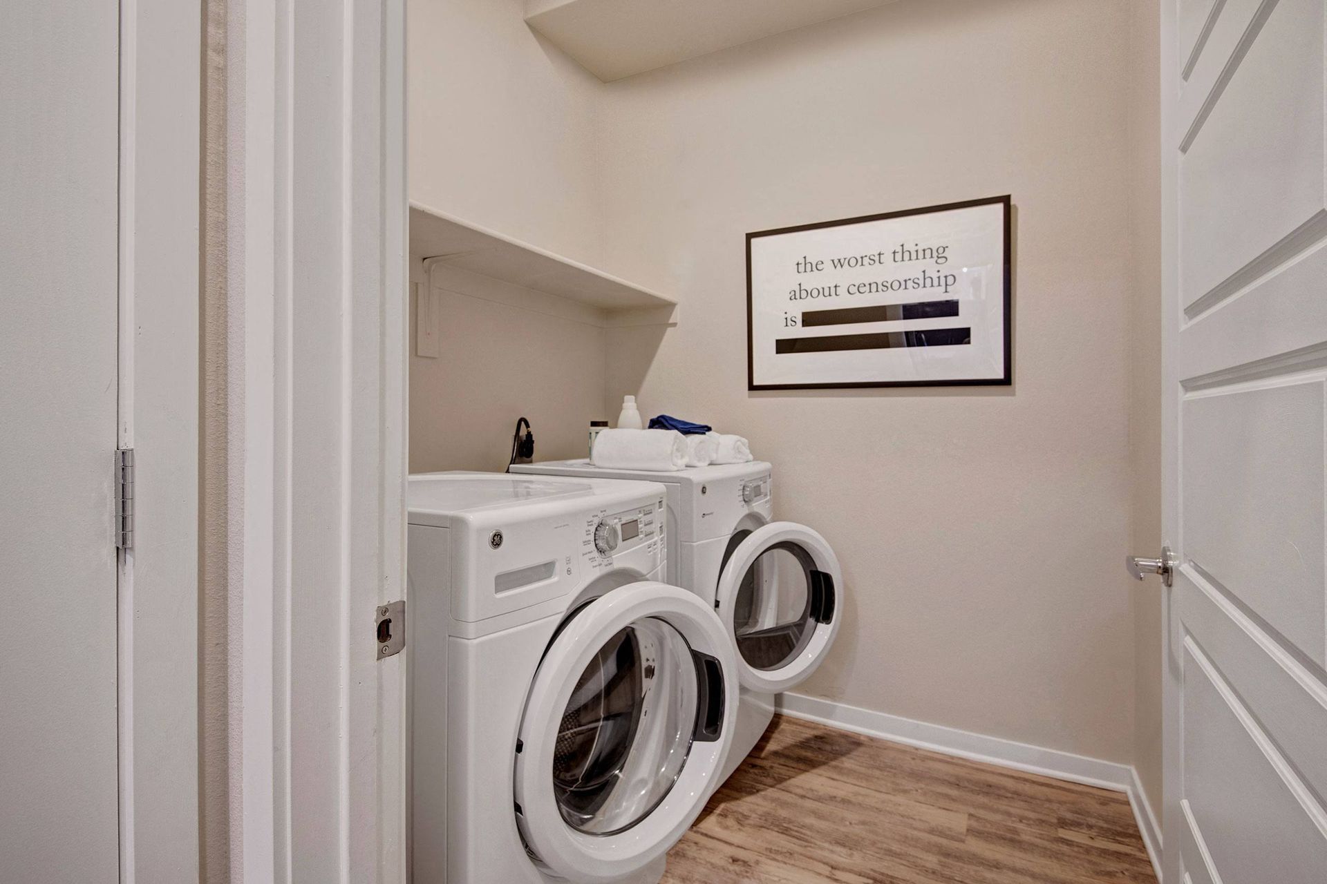 A small laundry room here at Park on Central Apartments with a washer and dryer, both doors open. Wall art with the phrase 