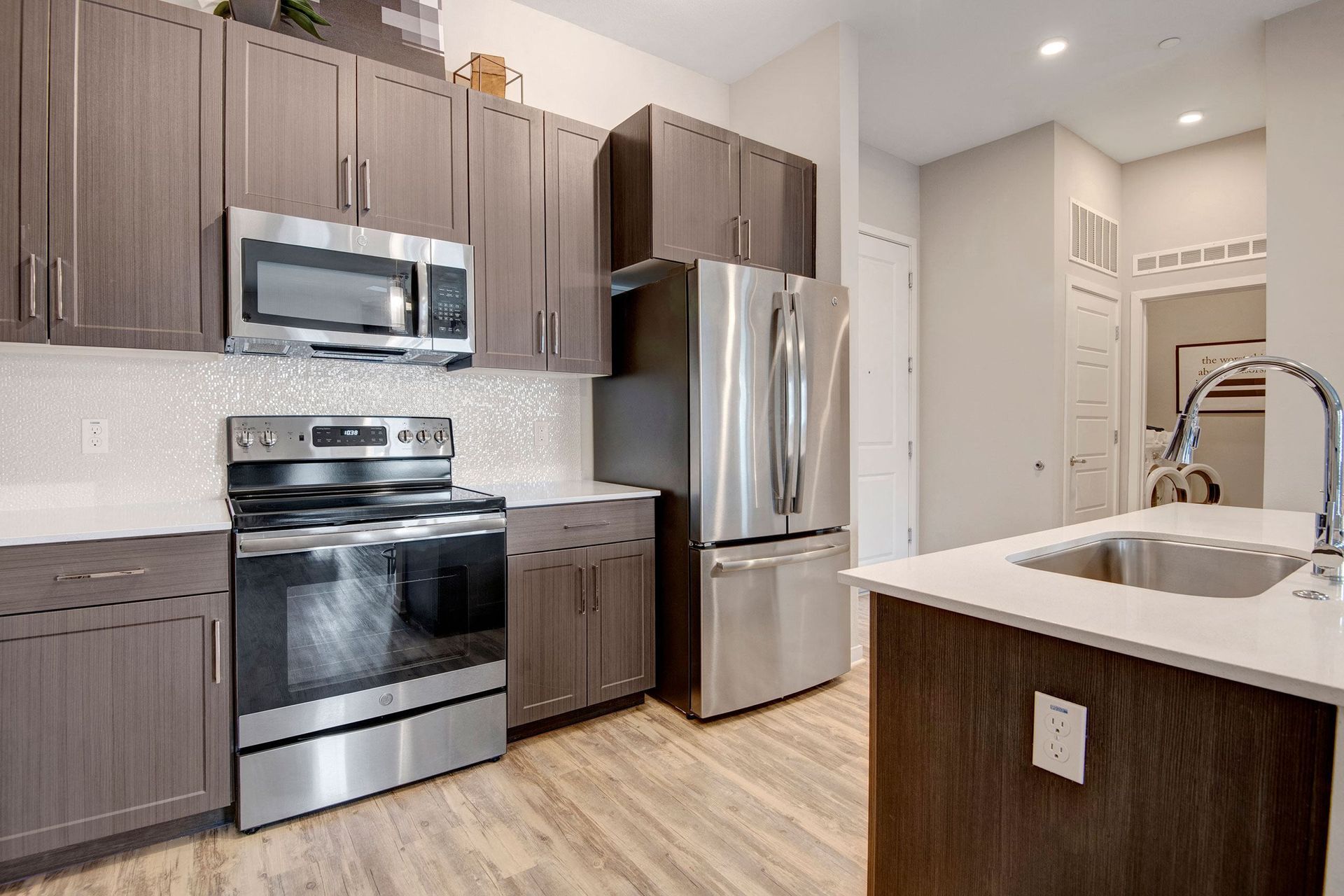 Modern kitchen here at Park on Central Apartments with dark wood cabinets, stainless steel appliances, and a sleek island with a sink. Warm wood flooring adds a cozy touch.