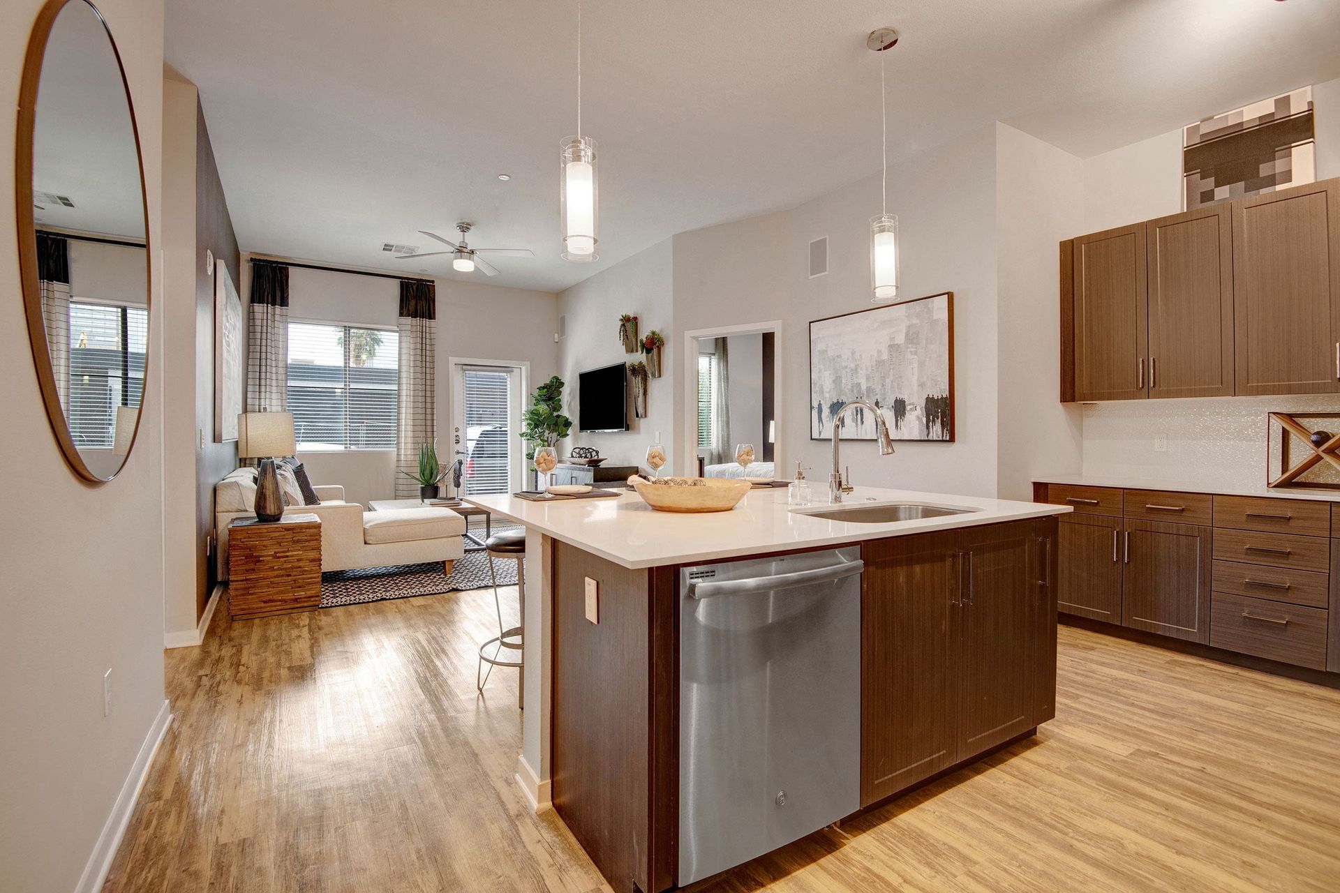 Modern kitchen and living room here at Park on Central Apartments with wooden floors, central island, pendant lights, and cozy seating area. Neutral tones create a warm, inviting space.