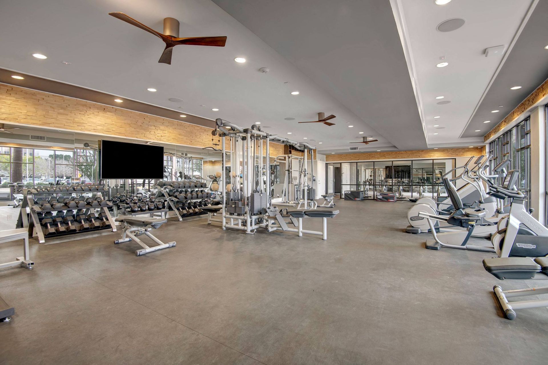 Spacious modern gym here at Park on Central Apartments with gray flooring, mirrored walls, and high ceiling. Equipped with free weights, exercise machines, and cardio equipment. Bright, airy atmosphere.