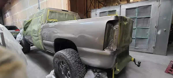 Gray pickup truck masked with green plastic in a paint booth or auto body shop