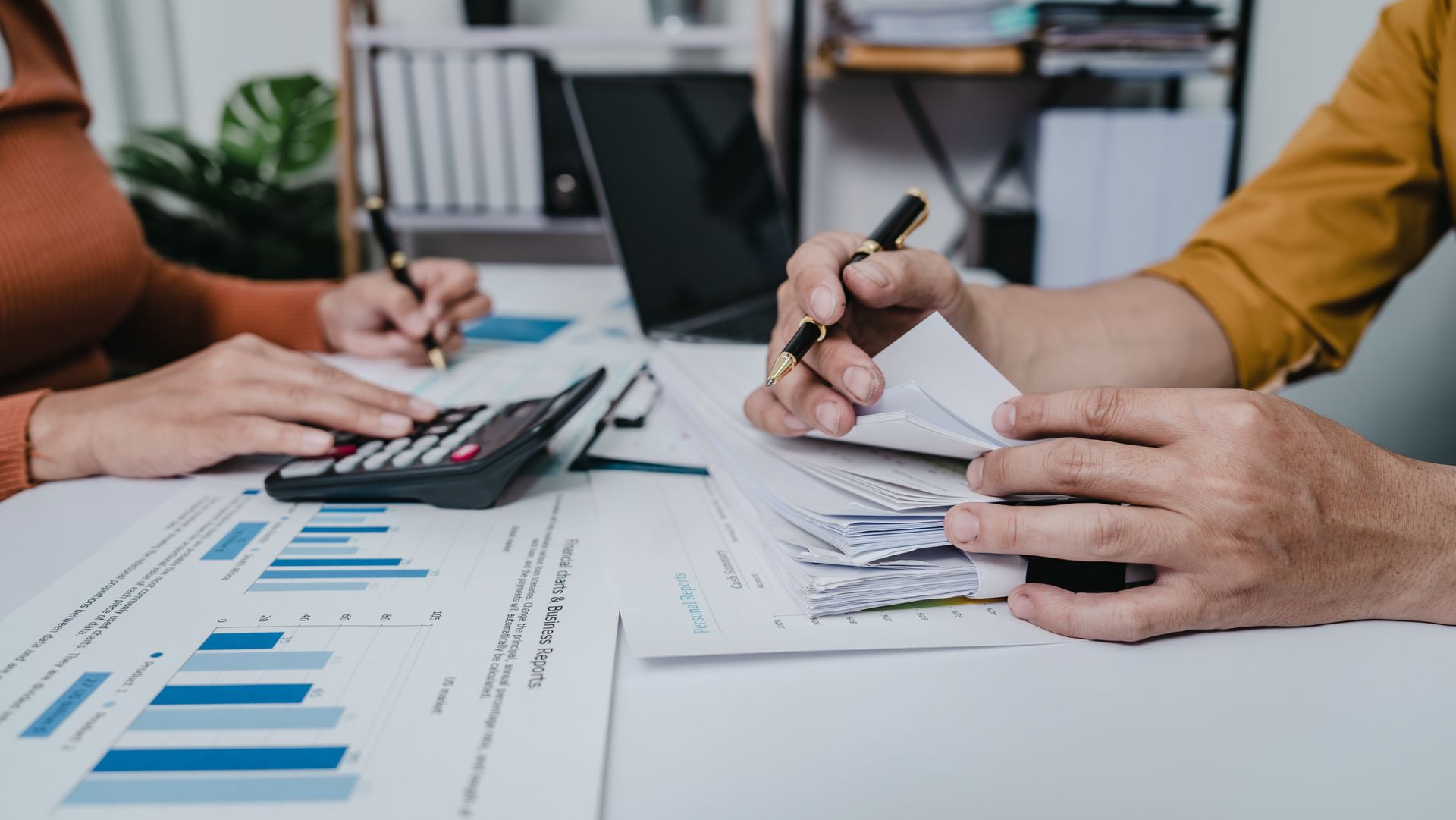 Hands writing on financial charts and calculator during a business meeting with a laptop nearby