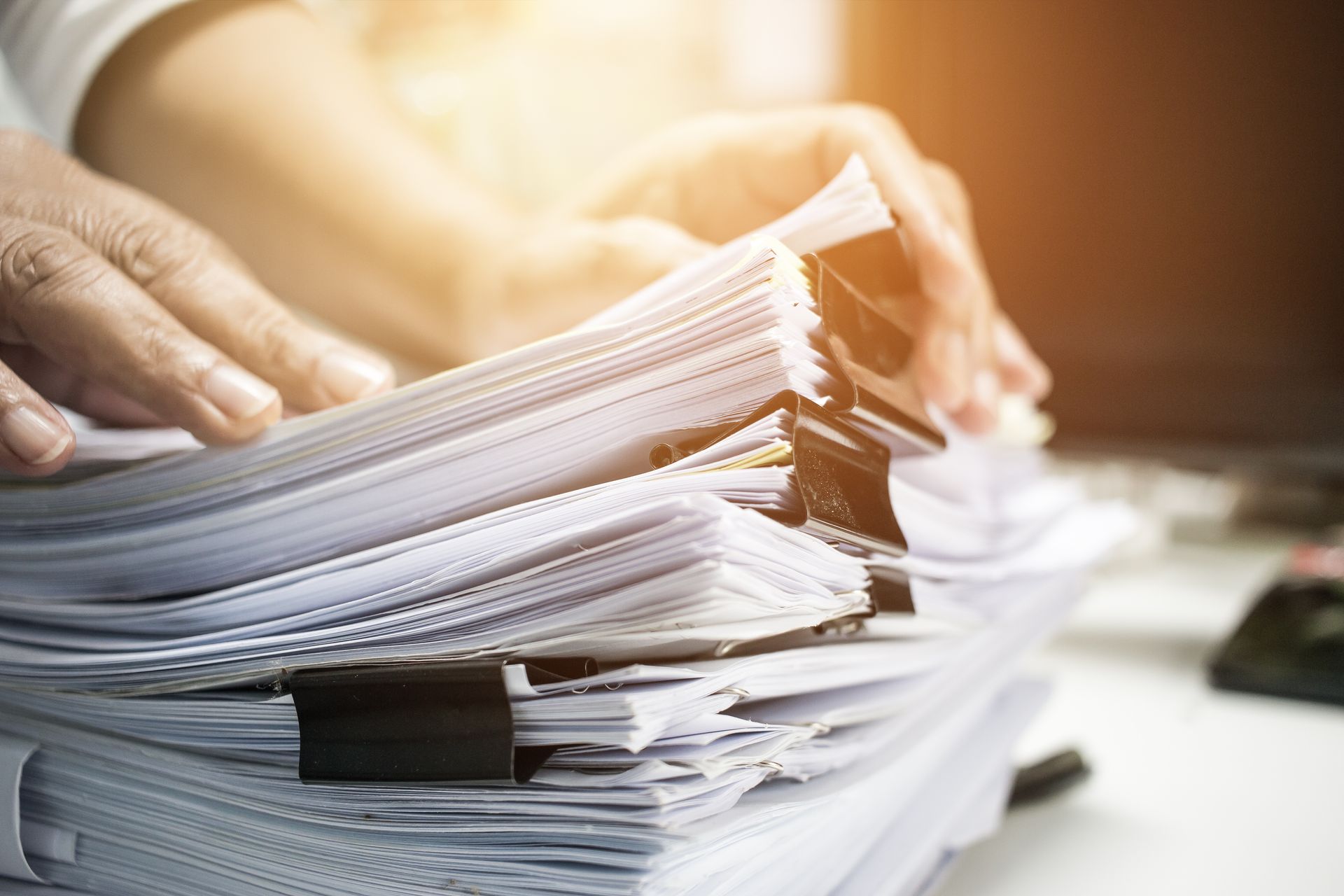 Hands sorting a large stack of paper documents on a desk