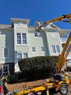 A worker in a yellow lift is painting the light green exterior of a two-story building on a sunny day.