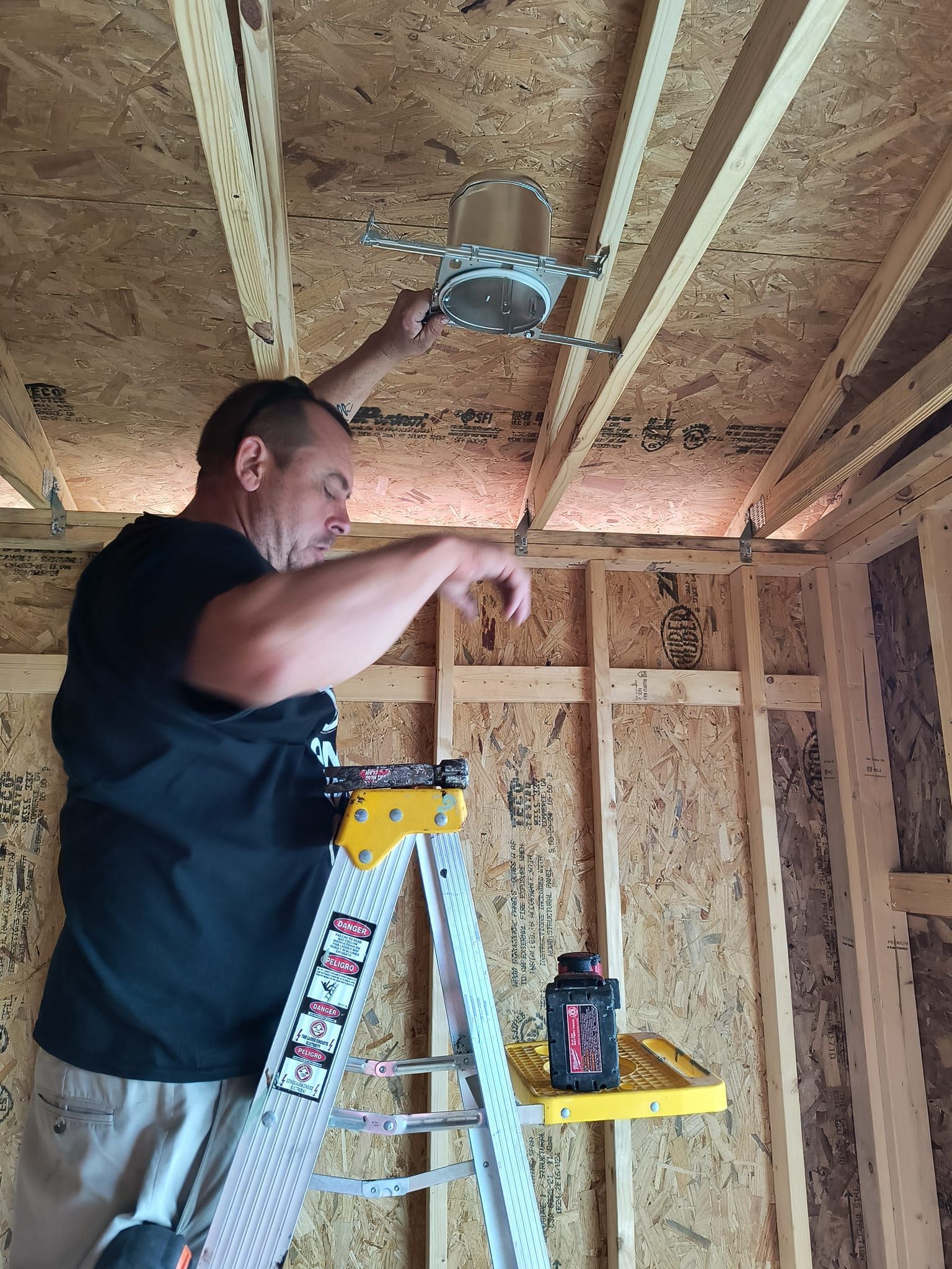 Man on ladder installs recessed light in unfinished room.