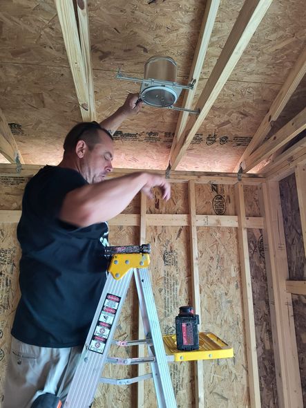 Man on ladder installs recessed light in unfinished room.