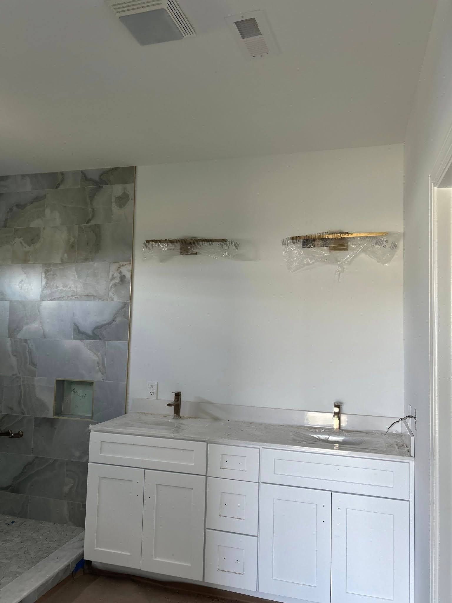 Bathroom under construction: white cabinets, gold light fixtures, marble tile, and a sink.