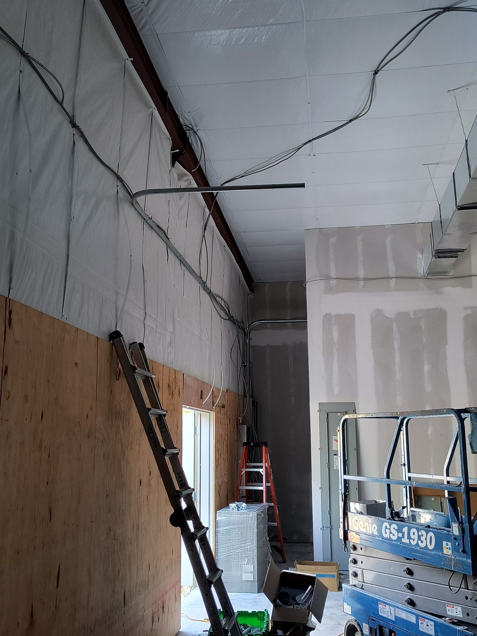 Interior of a construction site: electrical wiring installation along walls and ceiling, ladder leaning against the wall, blue lift.