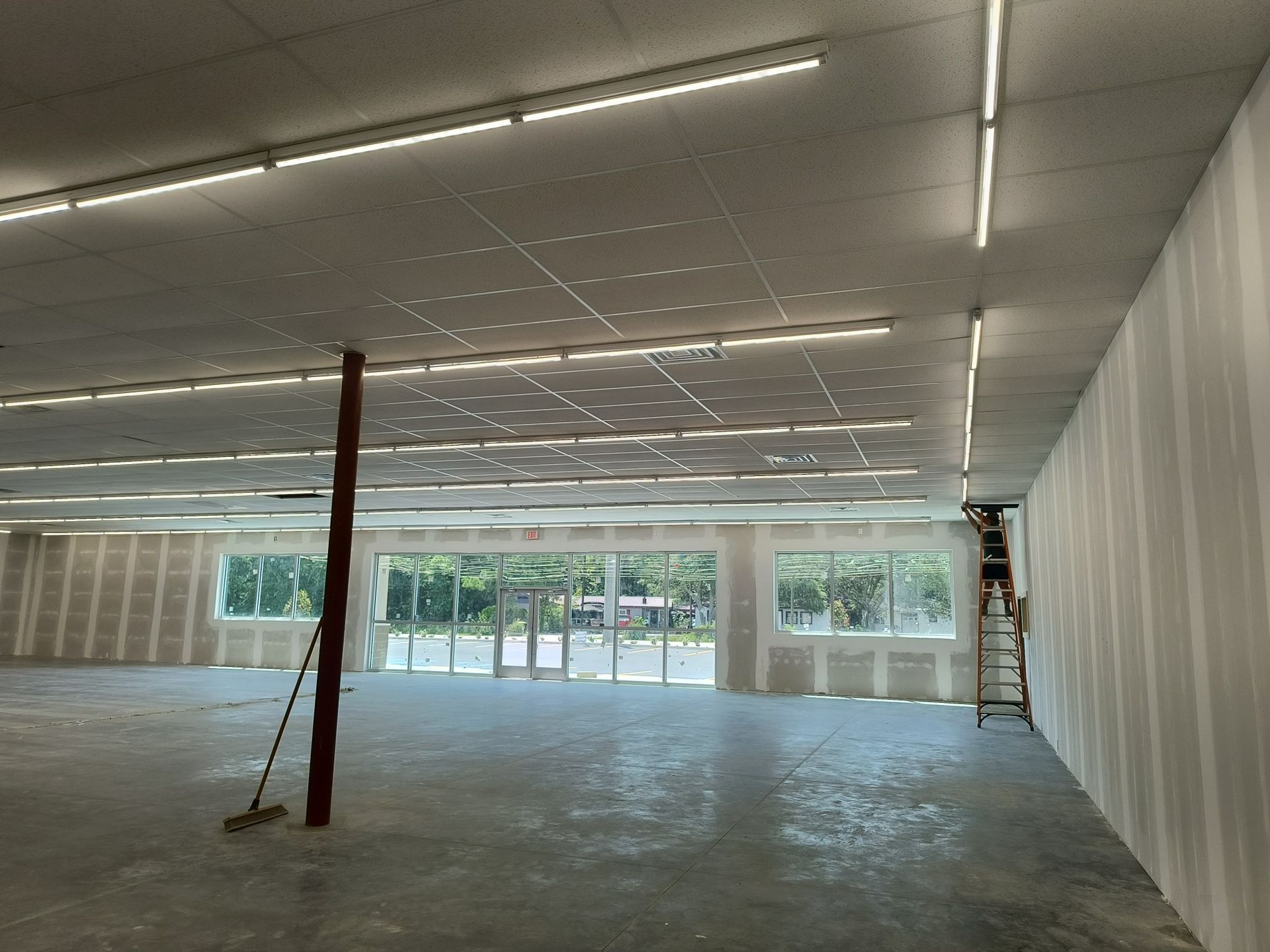 Interior of an unfinished commercial space with drywall, concrete floor, and fluorescent lighting.