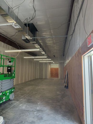Interior view of an unfinished commercial space with drywall, lighting, and a lift.