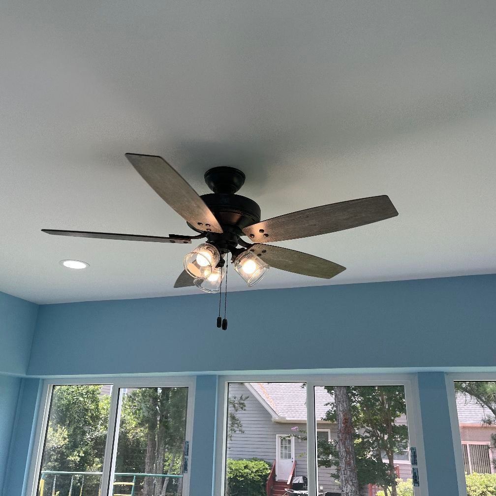 Ceiling fan with lights in a room with blue walls and large windows overlooking trees.