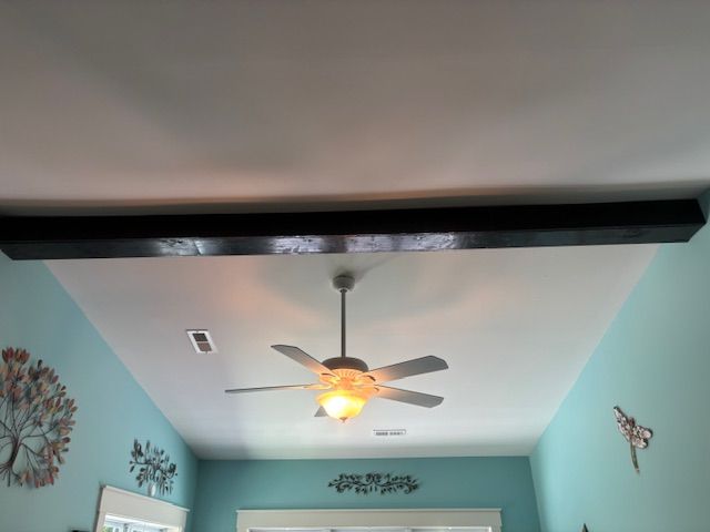 Ceiling fan with light on a white ceiling in a room with teal walls and black beams