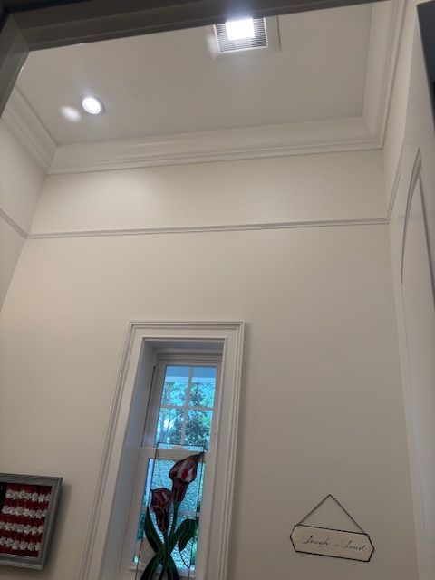 Tall white hallway with recessed ceiling lights, a small window, and wall decor.