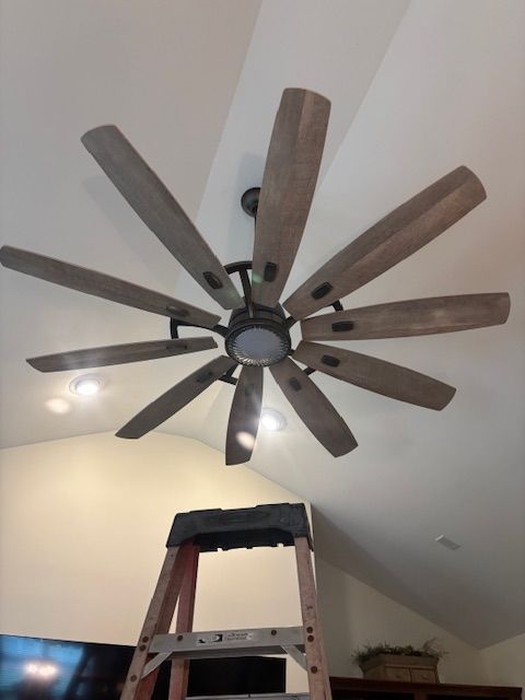 Ceiling fan with wooden blades above a ladder in a room with a vaulted ceiling