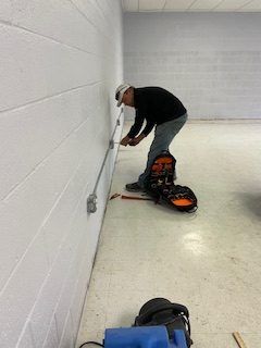 Electrician installing conduit on a white cinder block wall in a room with a light gray floor.
