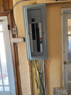 Electrical panel mounted on a yellow wall with exposed wires; door frames on either side.