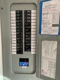 Electrical panel with rows of circuit breakers. Informational sheets attached to the door.