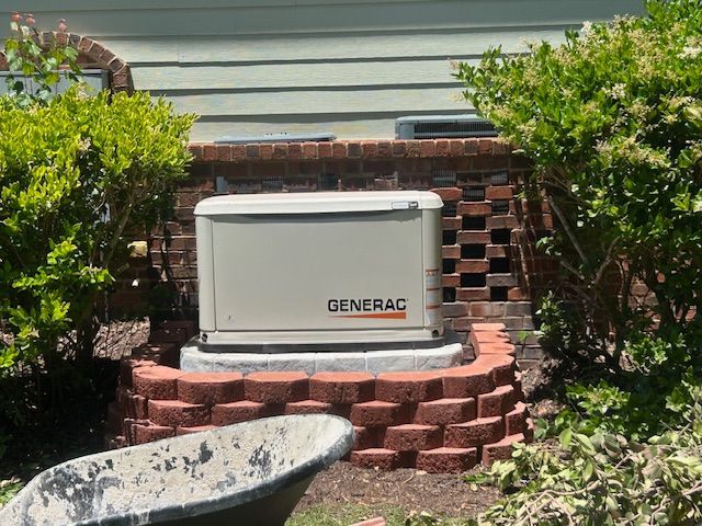 Generac backup generator on brick platform beside shrubs and house siding