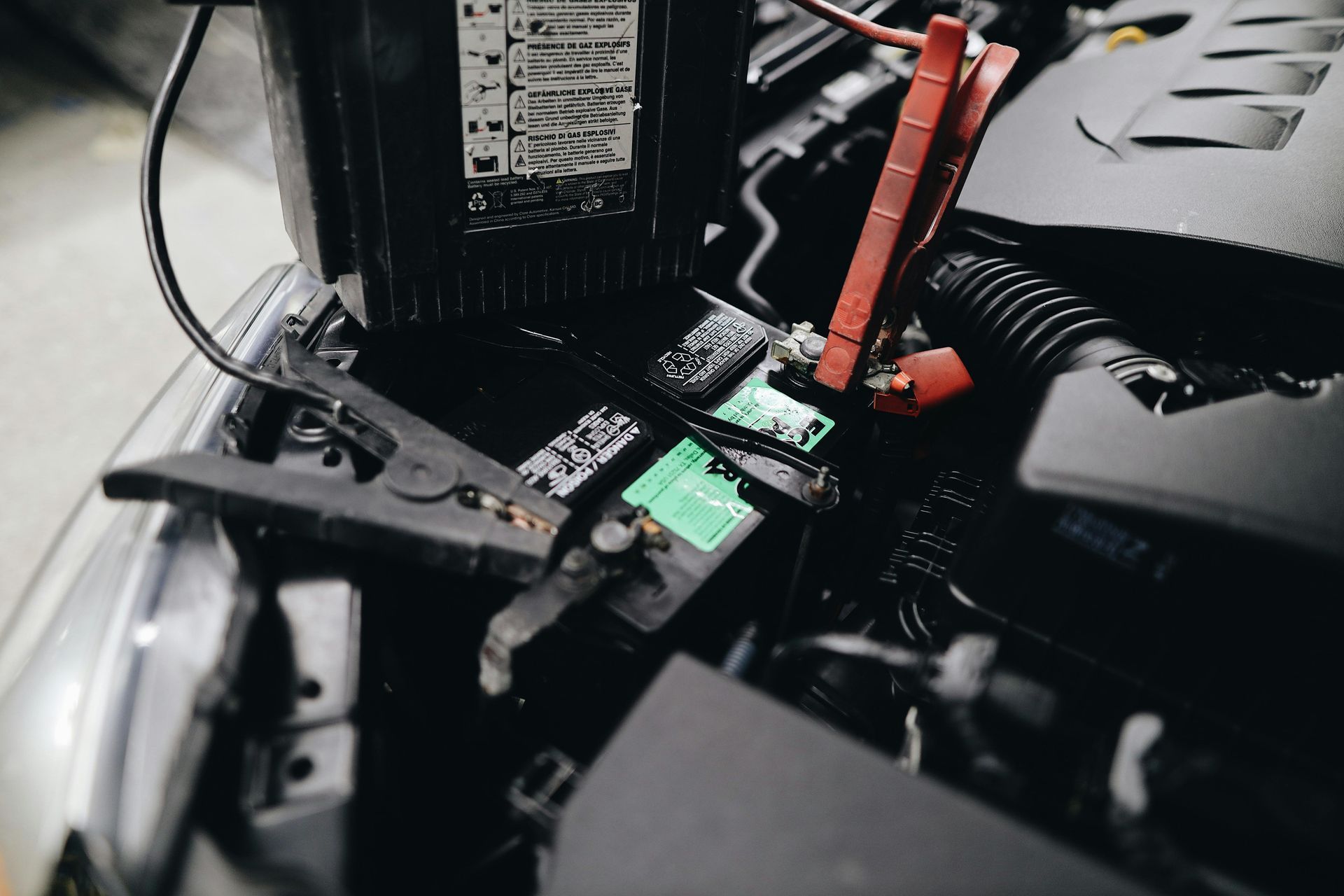 Close-up of a car battery with red and black jumper cables connected in an engine bay