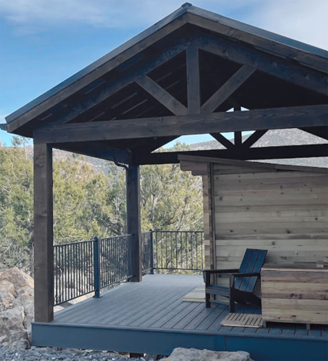 Wooden deck with a dark-stained roof, railings, and a chair, overlooking a valley.