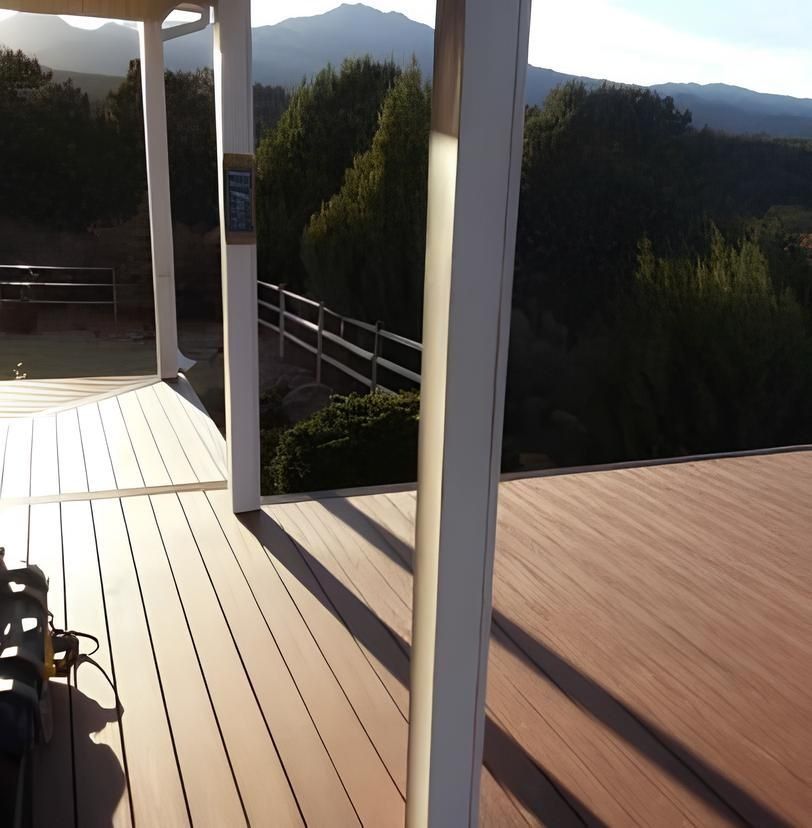 Wooden deck with white columns, overlooking a mountain and trees under a sunny sky.