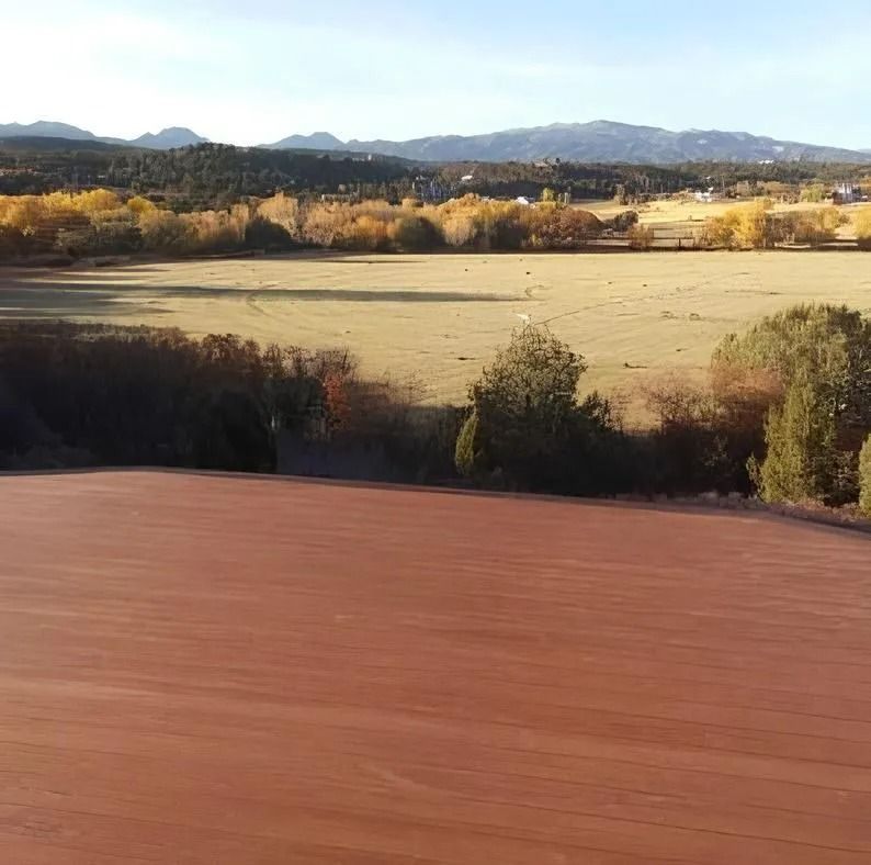 A scenic view of a field, surrounded by trees with autumn colors, mountains in the distance.