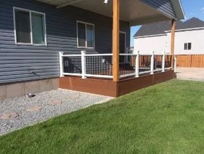 A home with a brown deck and white railing, gray siding, and green grass.