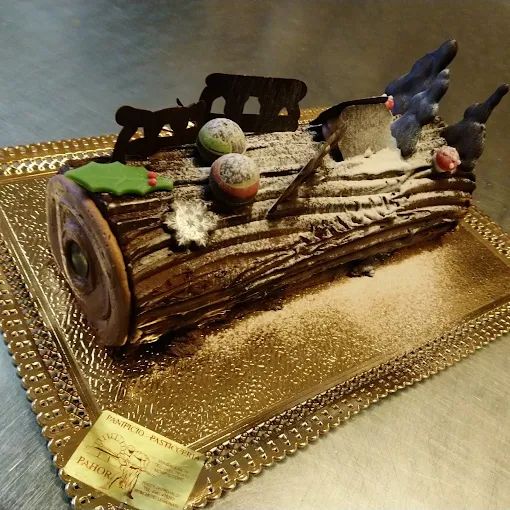 Tronchetto di Natale al cioccolato decorato con zucchero a velo, macaron e decorazioni di cioccolato su un vassoio dorato.