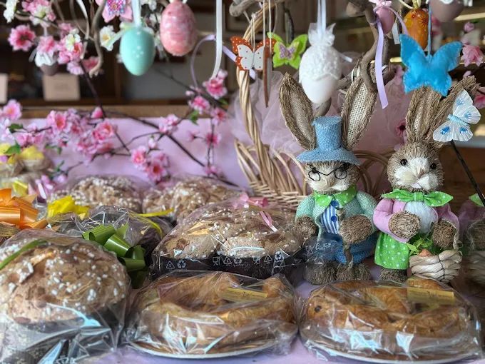 Dolcetti e decorazioni pasquali. Cestini, torte e statuine di coniglietti con uova di Pasqua e fiori, esposti in una vetrina di pasticceria.