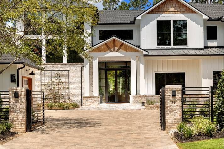A large white house with a brick driveway and a fence in front of it.