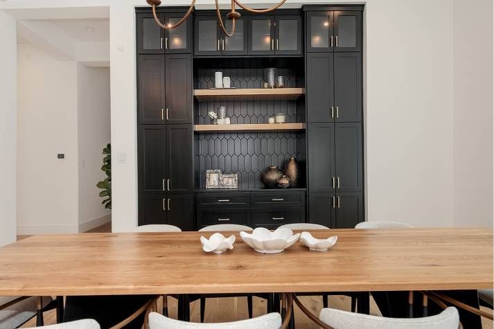A dining room with a wooden table and chairs and black cabinets.