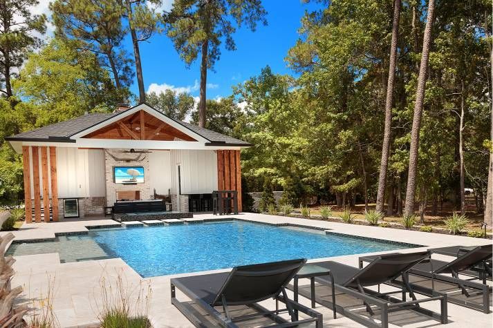 There is a large swimming pool in the backyard of a house surrounded by trees.