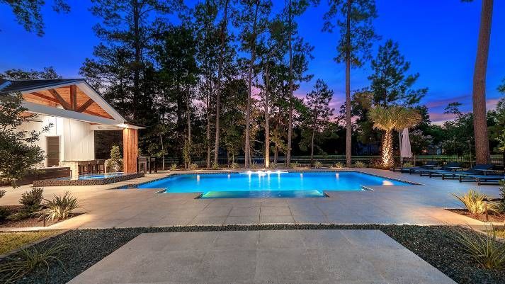 There is a large swimming pool in the backyard of a house surrounded by trees.