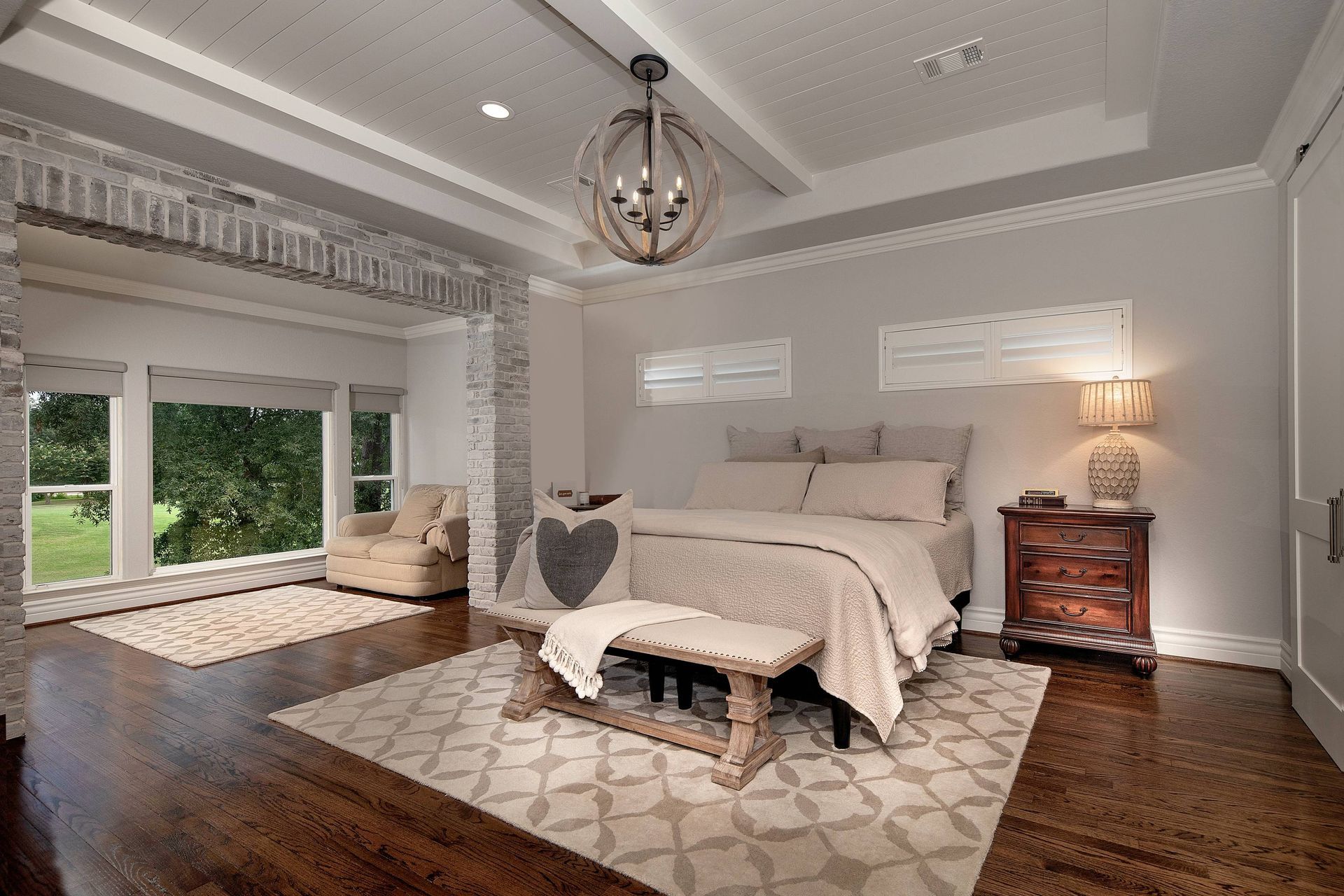 A bedroom with a bed , nightstand , chair , rug and a chandelier.