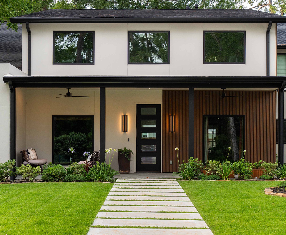 Modern house with white walls, black trim, and a concrete path leading to the front door.