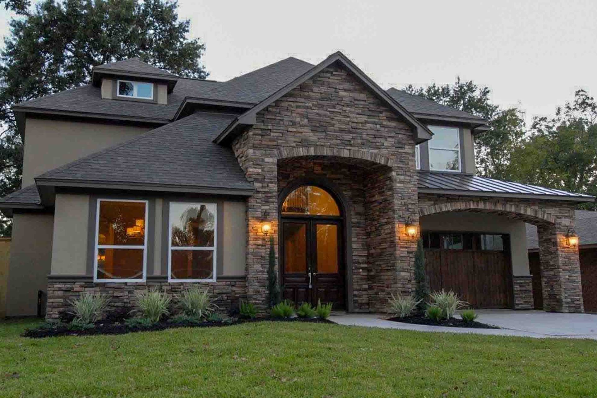 A large house with a stone facade is sitting on top of a lush green lawn.