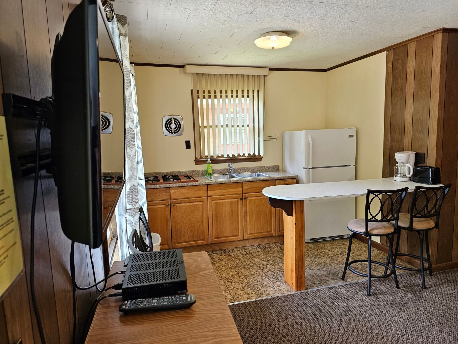 Small kitchen and dining area with wooden cabinets, white fridge, and a table by the window.
