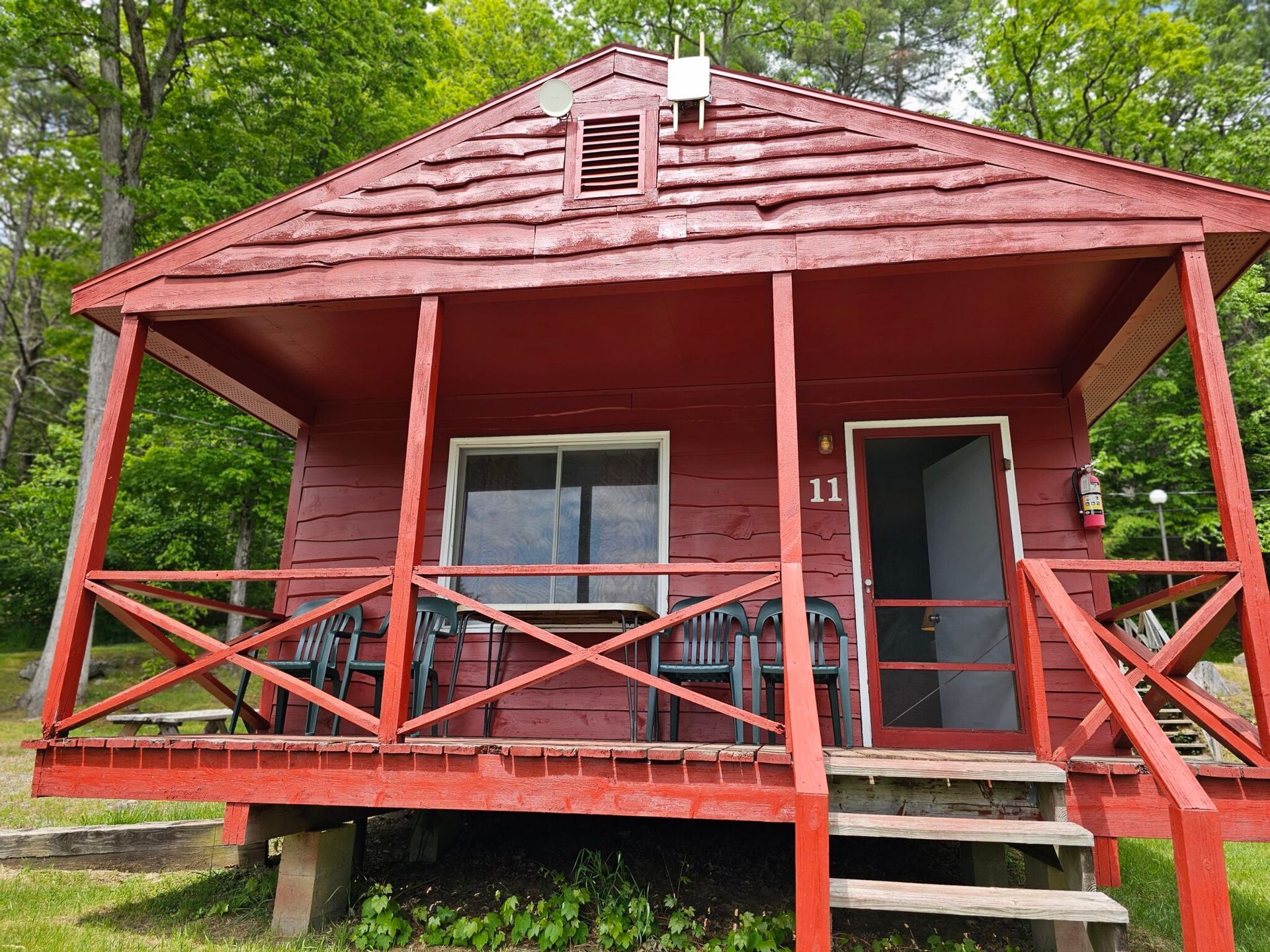 Red wooden cabin with porch, steps, and green-trimmed doors in a wooded area