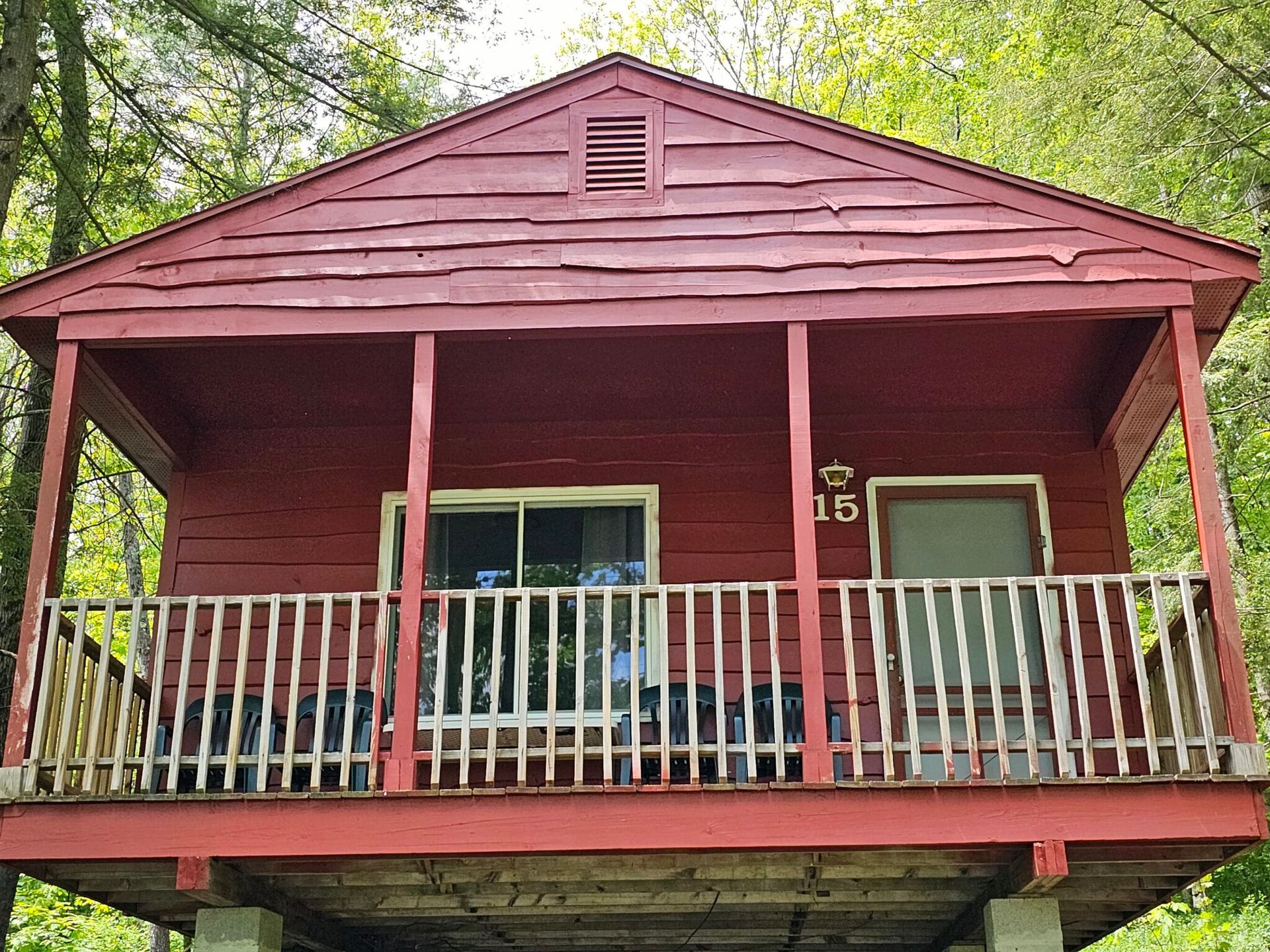 Red wooden cabin porch with white railing and trees in the background