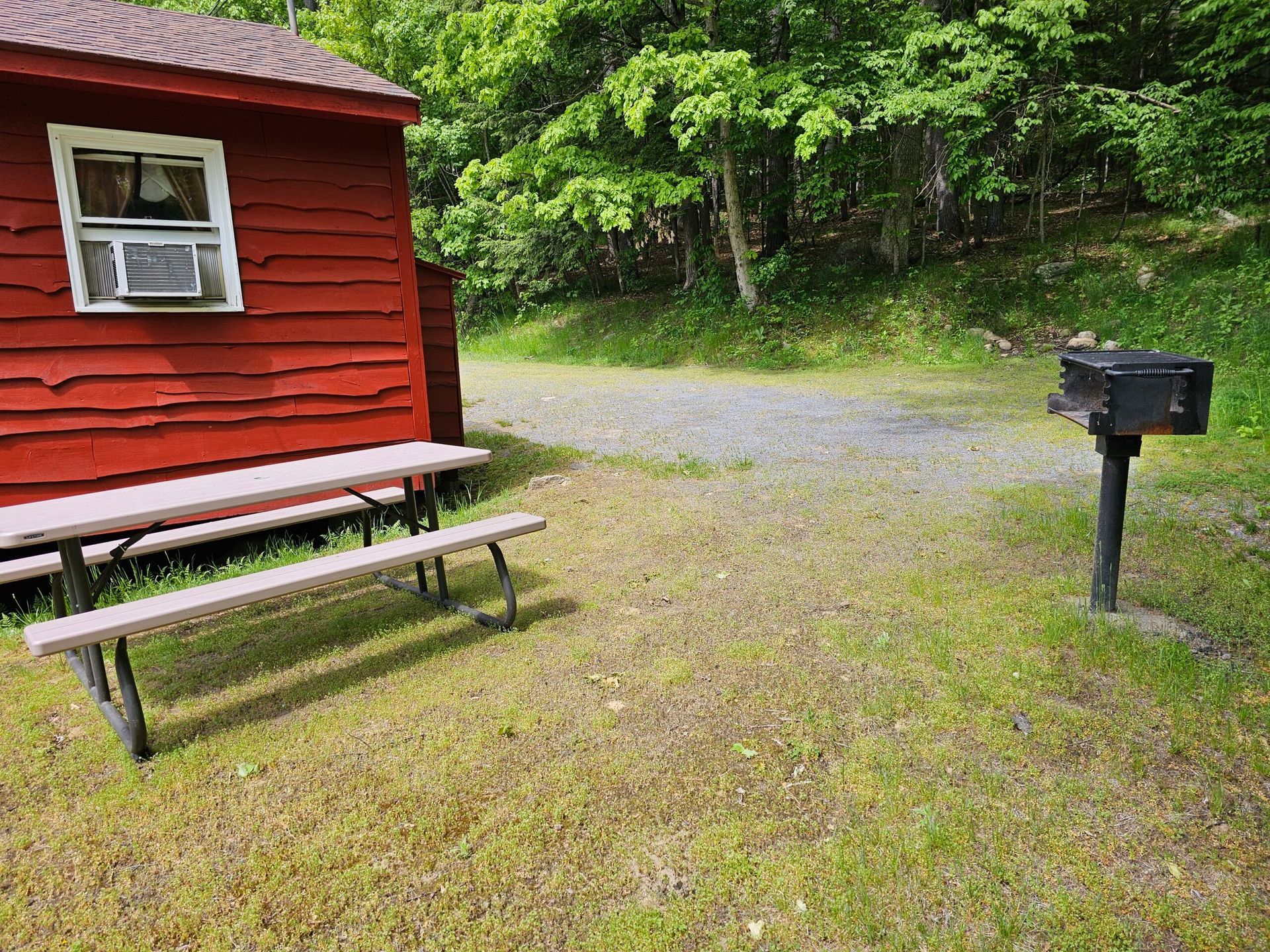 Red cabin with picnic table beside gravel driveway and black mailbox near wooded area