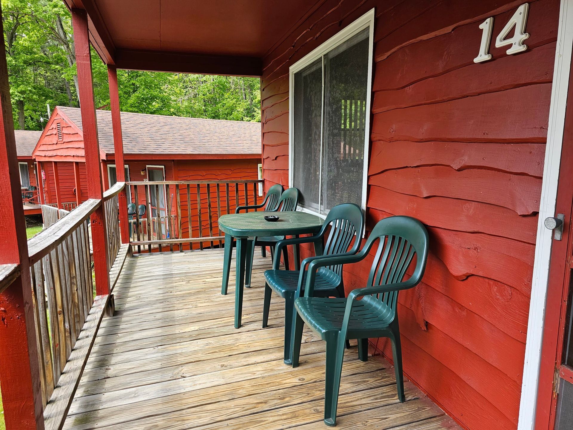 Red wooden porch with table and chairs beside a screened door, house number 14 visible