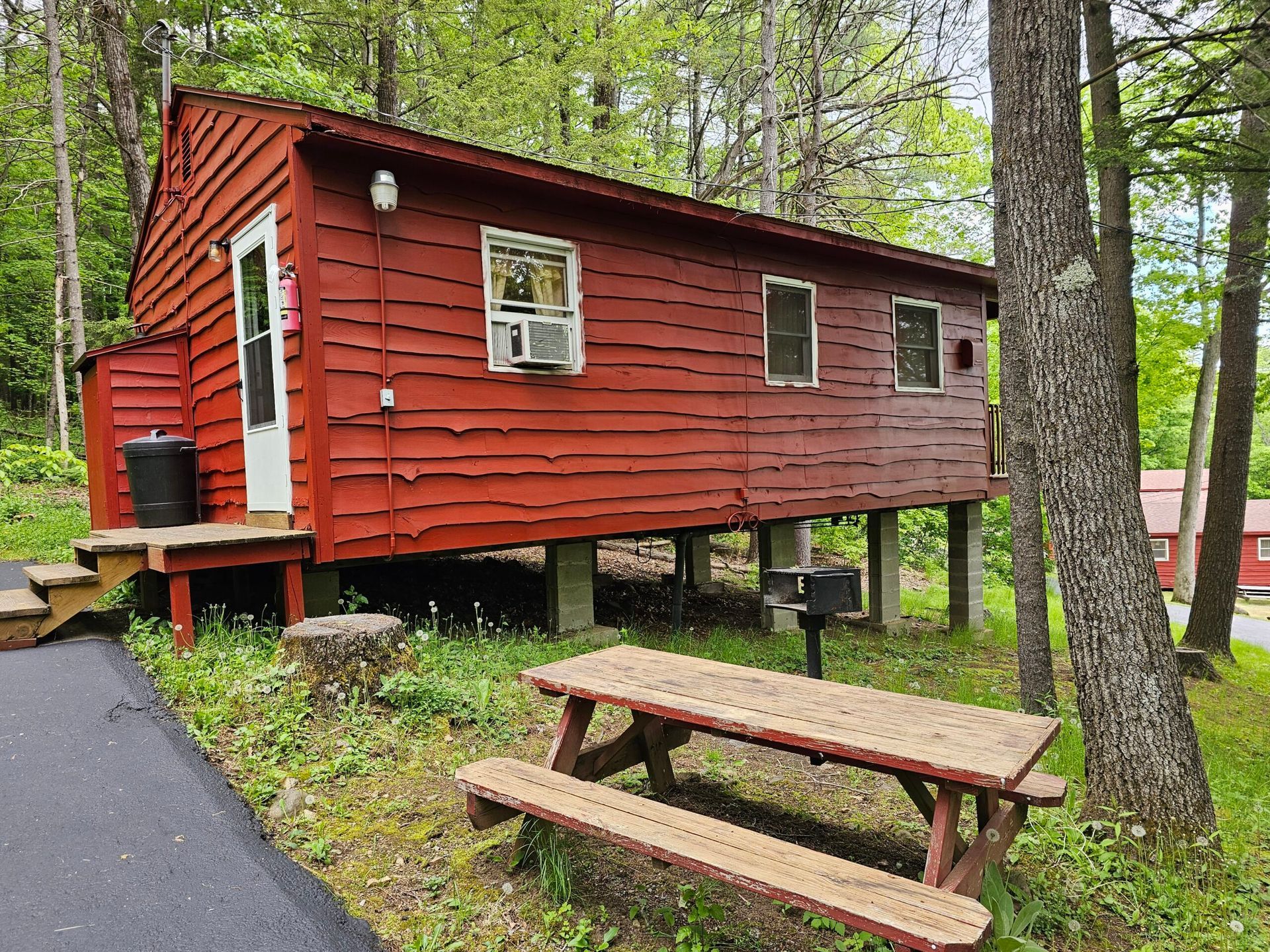 Red cabin in a wooded campsite with a picnic table and paved path