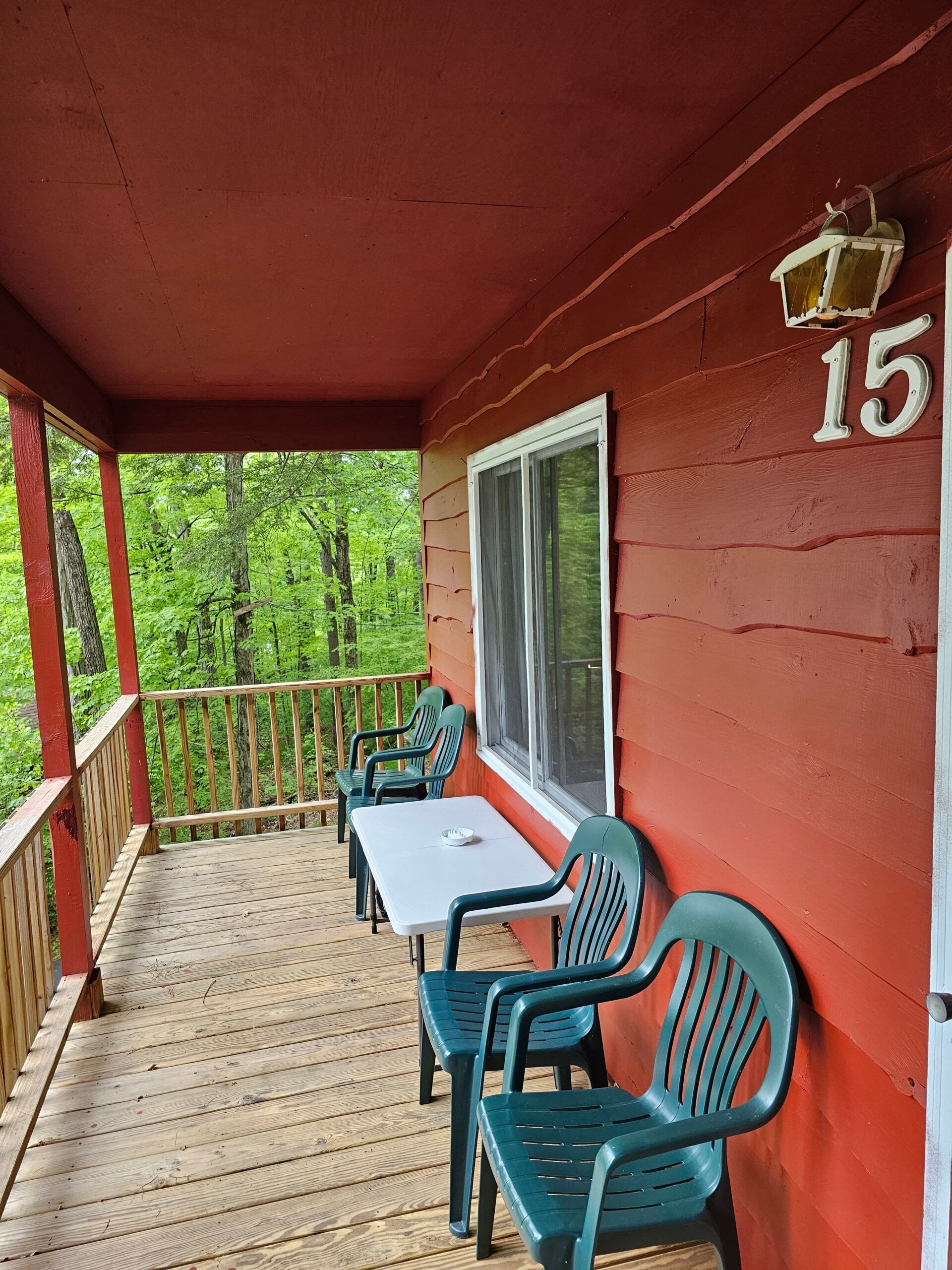 Covered cabin porch with red walls, two teal chairs, and a window overlooking trees and a wooden railing.