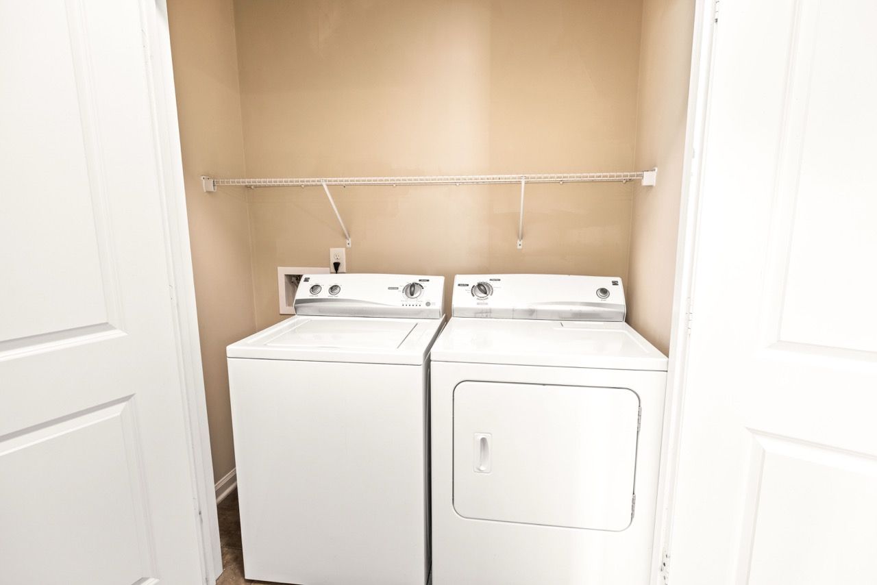 Laundry closet with a white side-by-side washer and dryer and a wire shelf above.