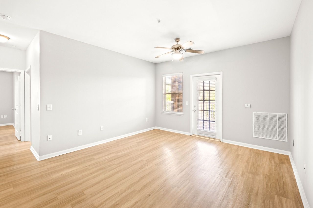 Empty living room with gray walls, light wood flooring, a ceiling fan, and a glass door to the outdoors.