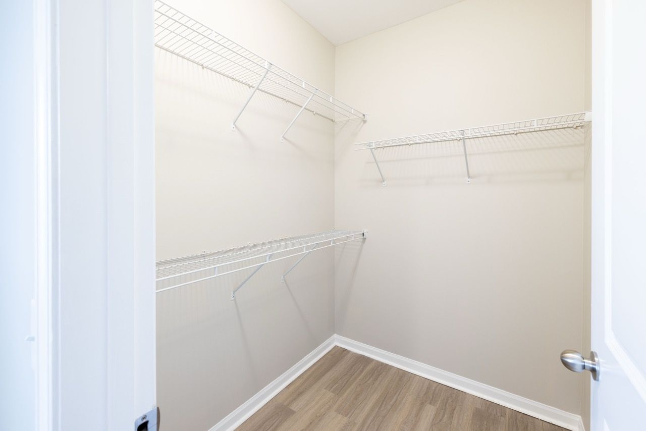 Walk-in closet with white wire shelving along two walls and a light wood floor.