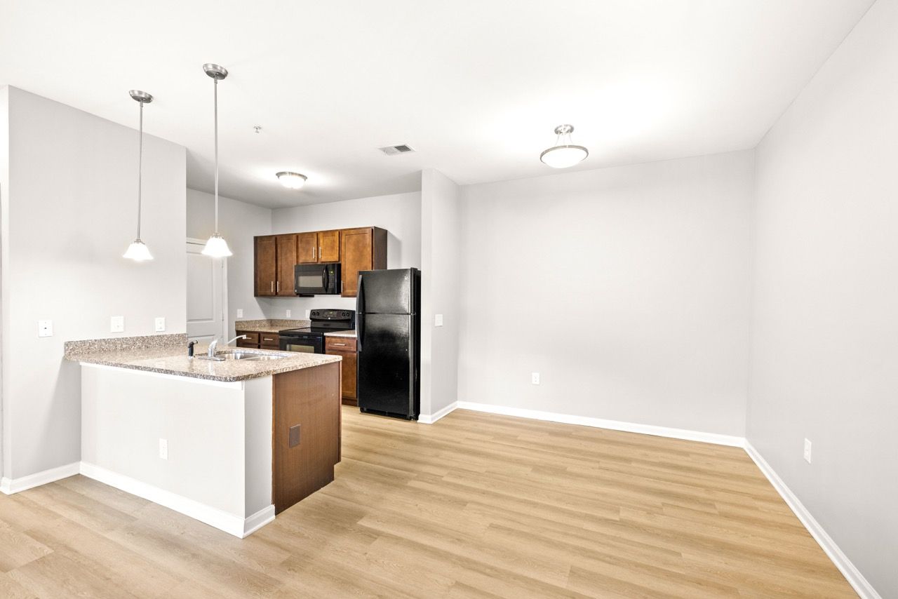 Open-concept apartment kitchen with granite island, wood cabinets, and black appliances.