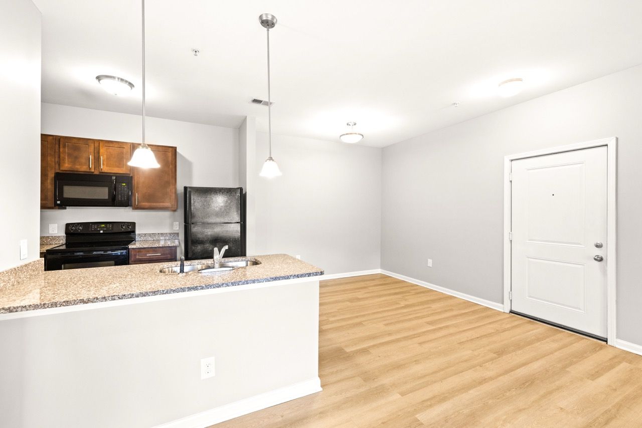 Open-concept kitchen with granite island, sink, and dark appliances; light wood floors.